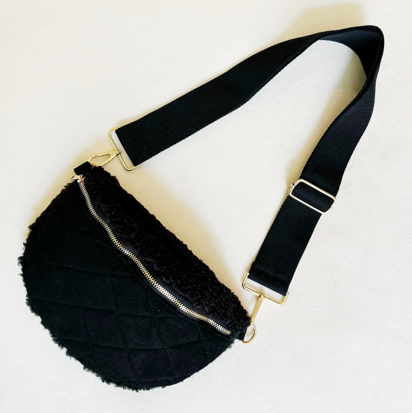 Black fur waist bag with gold zipper on a light beige background