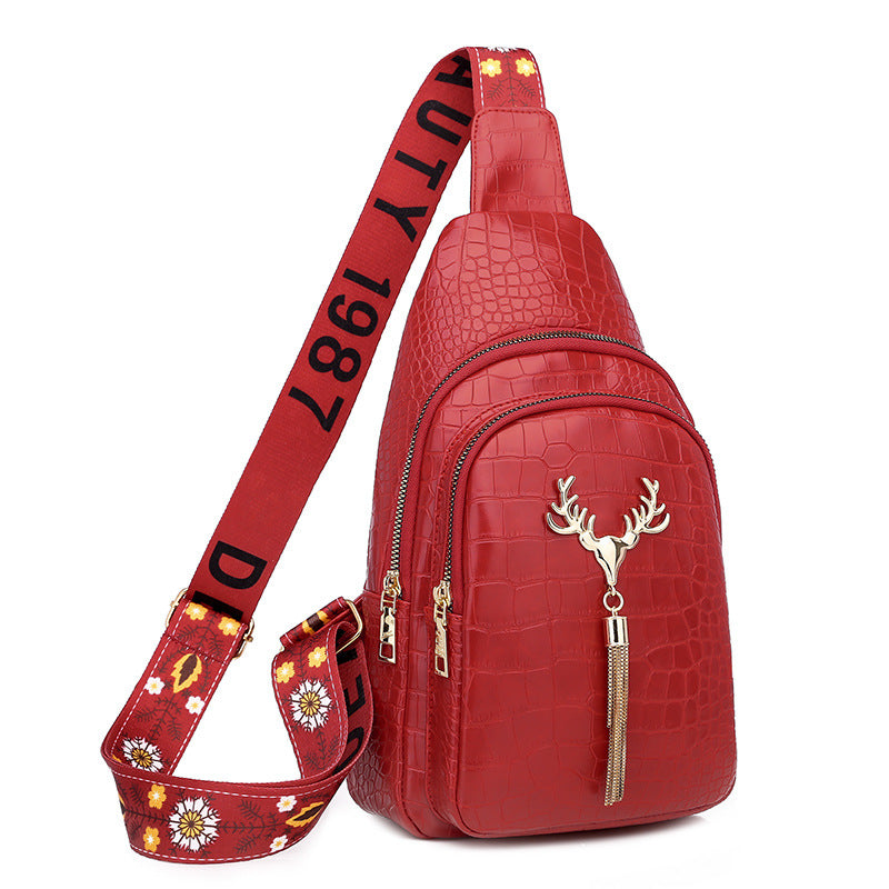 Red crocodile-patterned sling bag with deer emblem and decorative strap on a white background