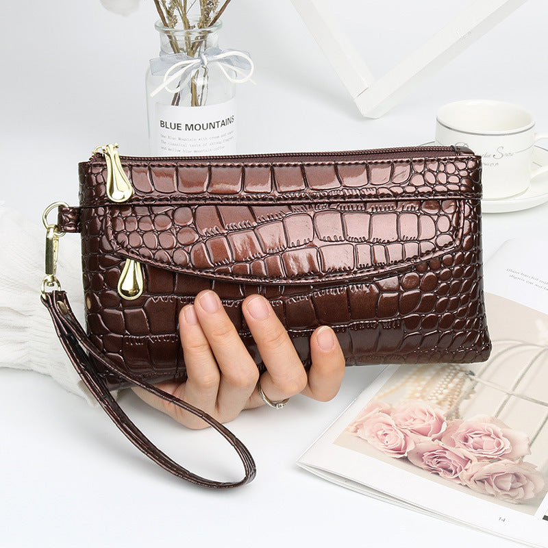 Brown crocodile-patterned clutch held by a hand on a light background