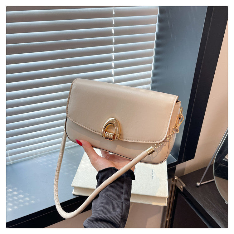 Beige handbag with gold clasp held by a hand against a window background