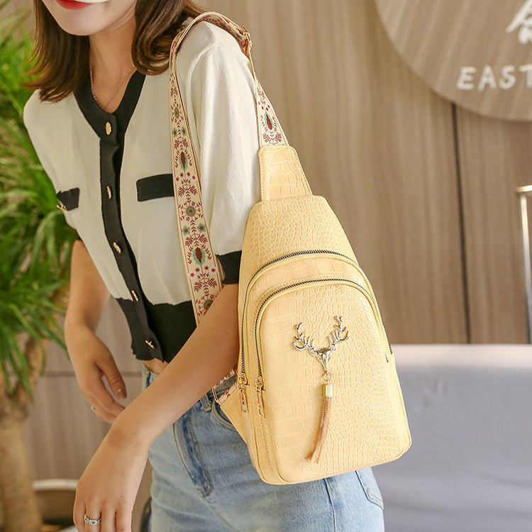 Person wearing a beige crossbody bag with a decorative strap in an indoor setting
