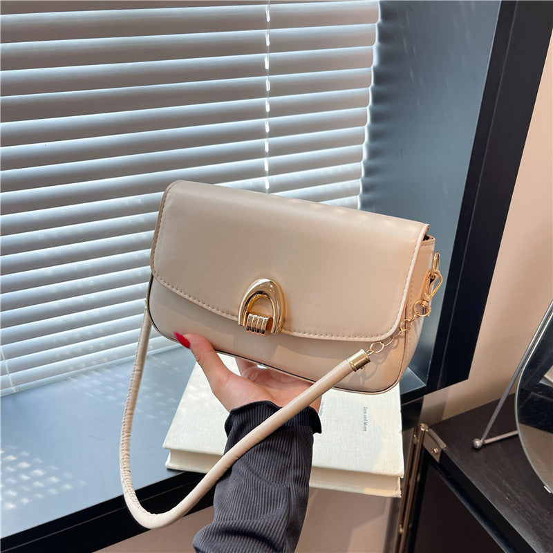 Beige handbag with gold accents held by a hand in front of a window.
