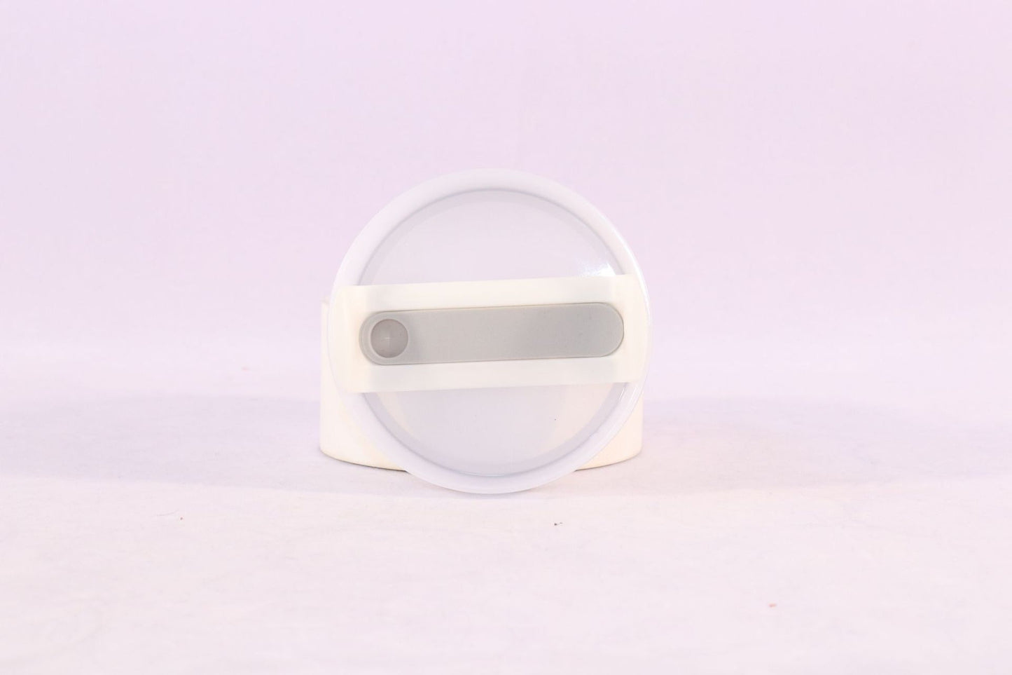Round white object with a central gray component on a light purple background