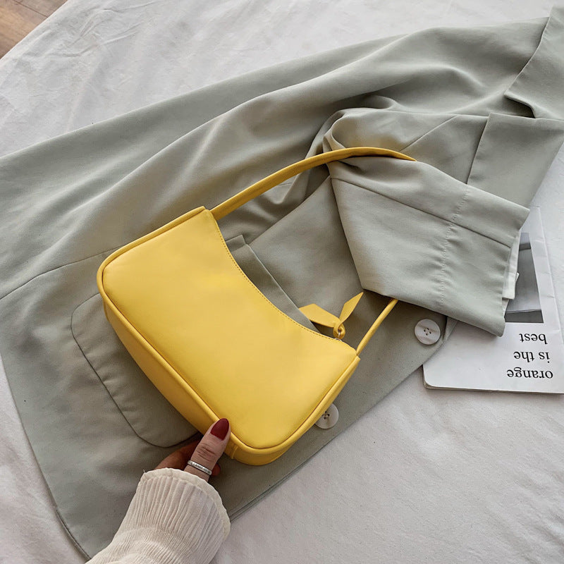 Yellow handbag held by a hand on a light gray fabric background