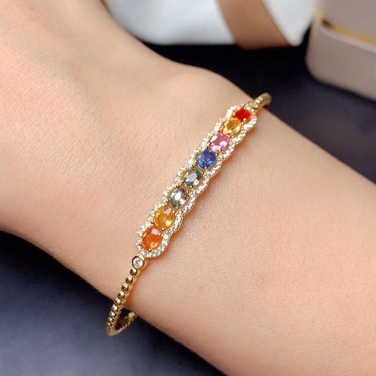 Gold bracelet with colorful gemstones on a wrist against a neutral background