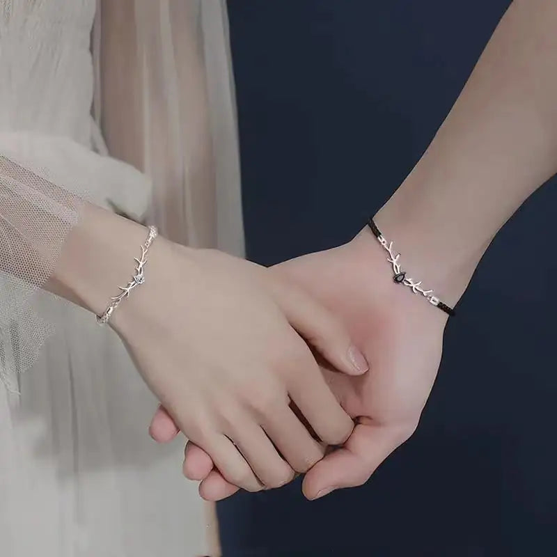 Two hands holding together with silver bracelets on a dark background