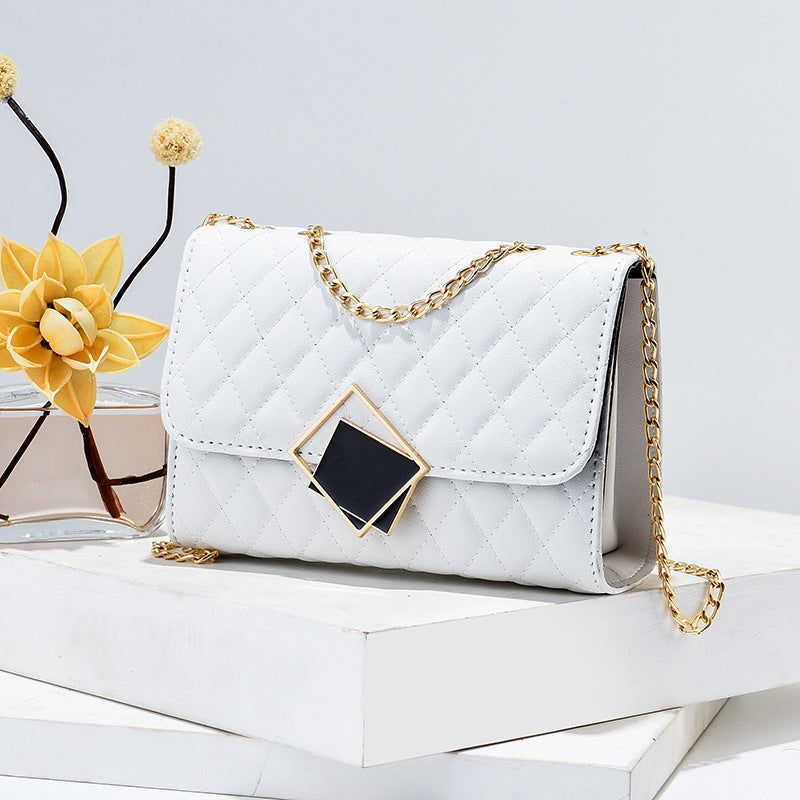 White handbag with gold chain on a white surface with a yellow flower in the background