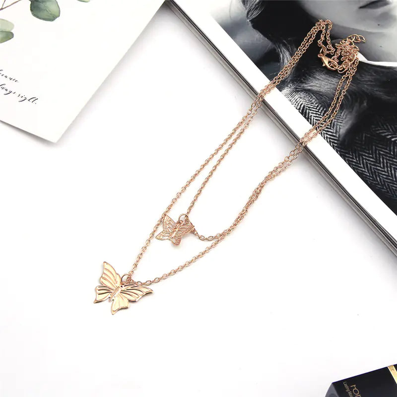 Rose gold butterfly necklace on a white surface with a magazine in the background