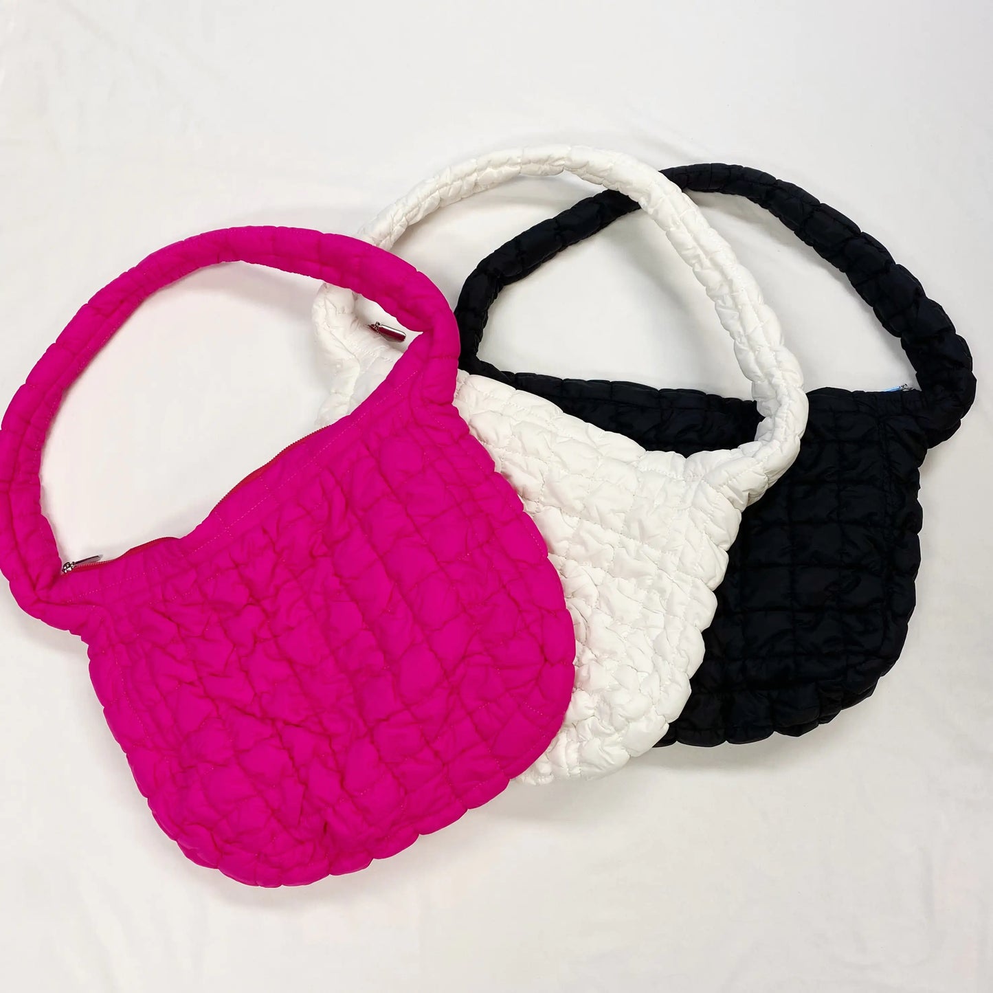 Three textured handbags in pink, white, and black on a light gray background