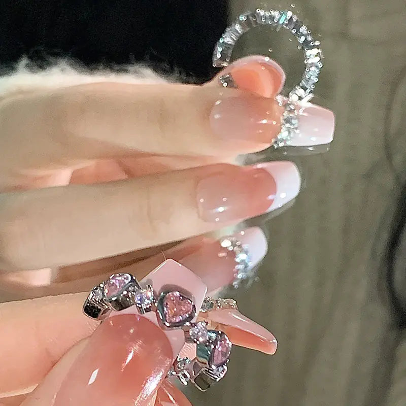 Clear dental aligner with pink heart-shaped gemstones held by a hand with pink nail polish.