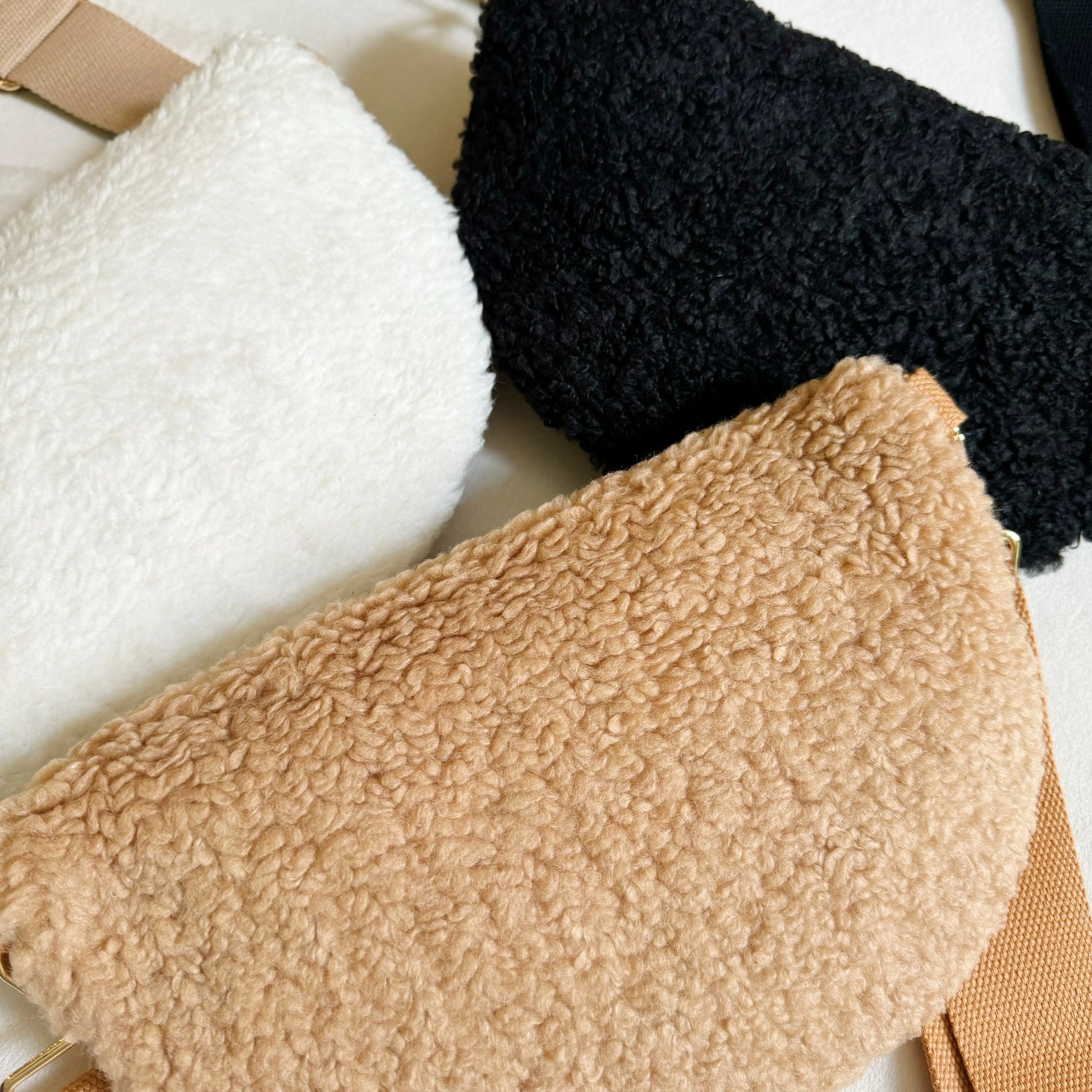 Three textured pouches in white, black, and beige on a light background