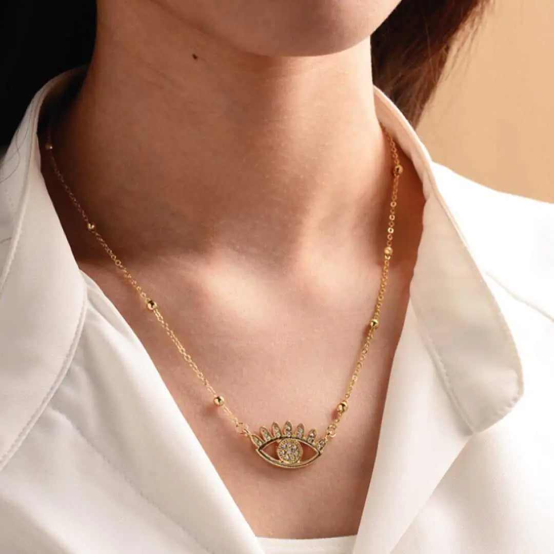 Gold necklace with an eye design worn by a person in a white shirt