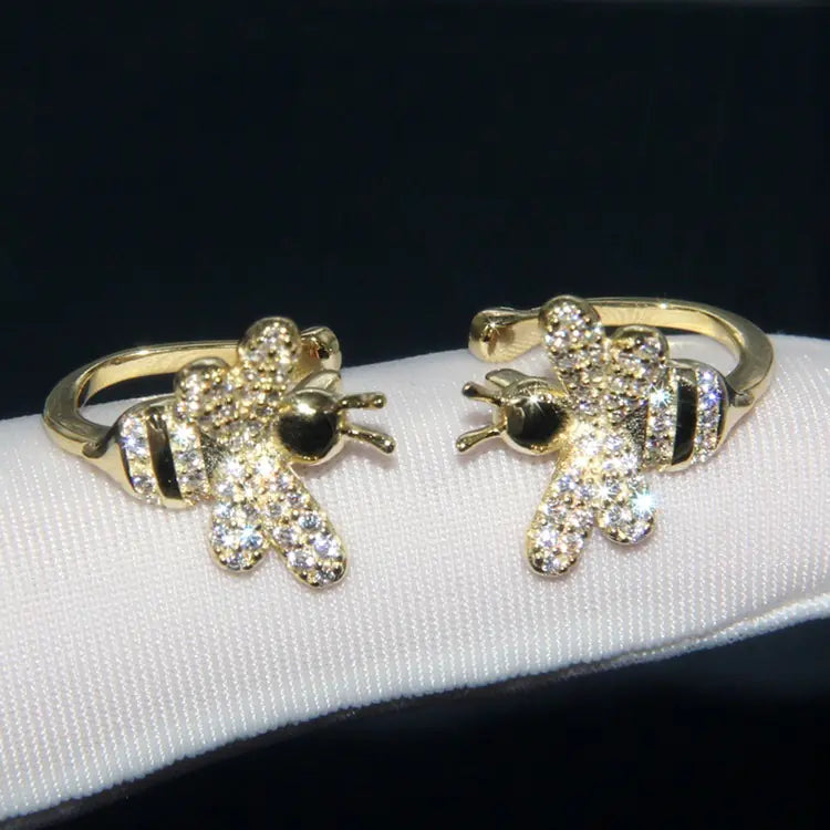 Gold bee-shaped earrings with clear gemstones on a white cushion against a black background