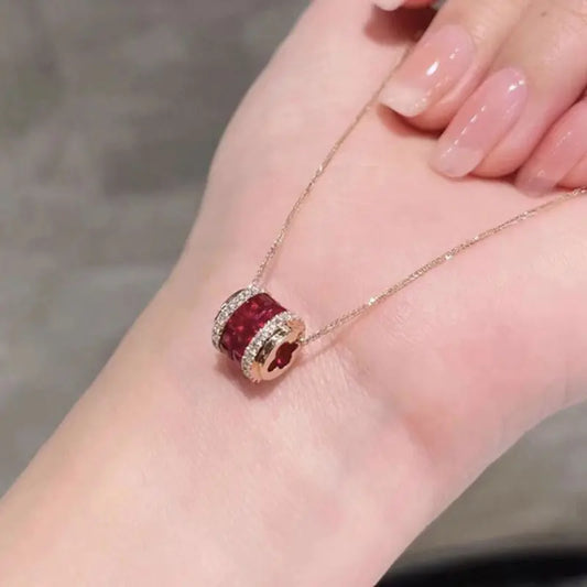 Red pendant on a gold chain held in a hand with pink nail polish.