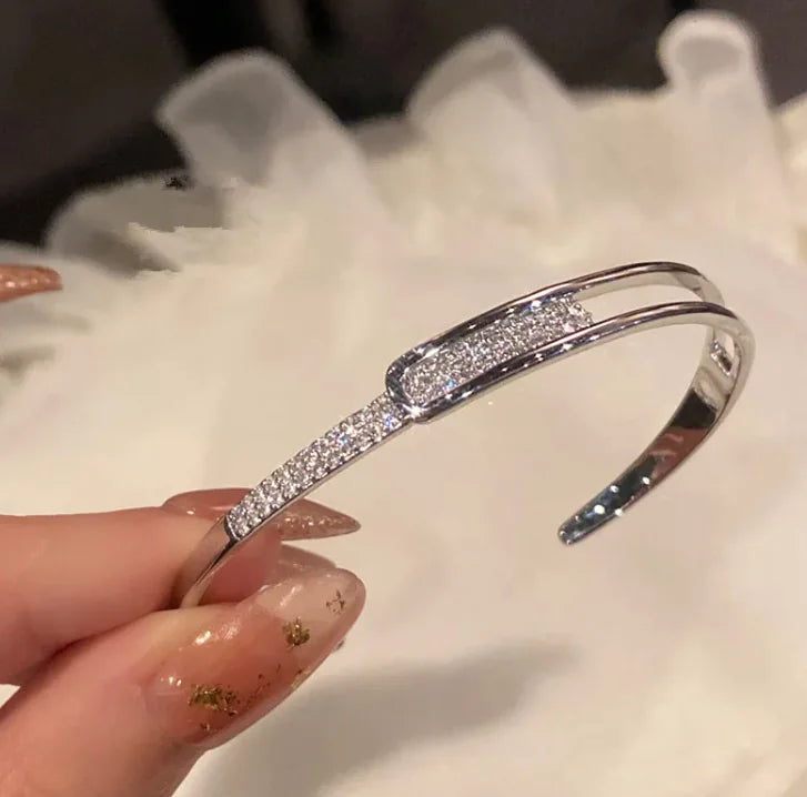 Silver bracelet with clear stones held by a hand on a white surface