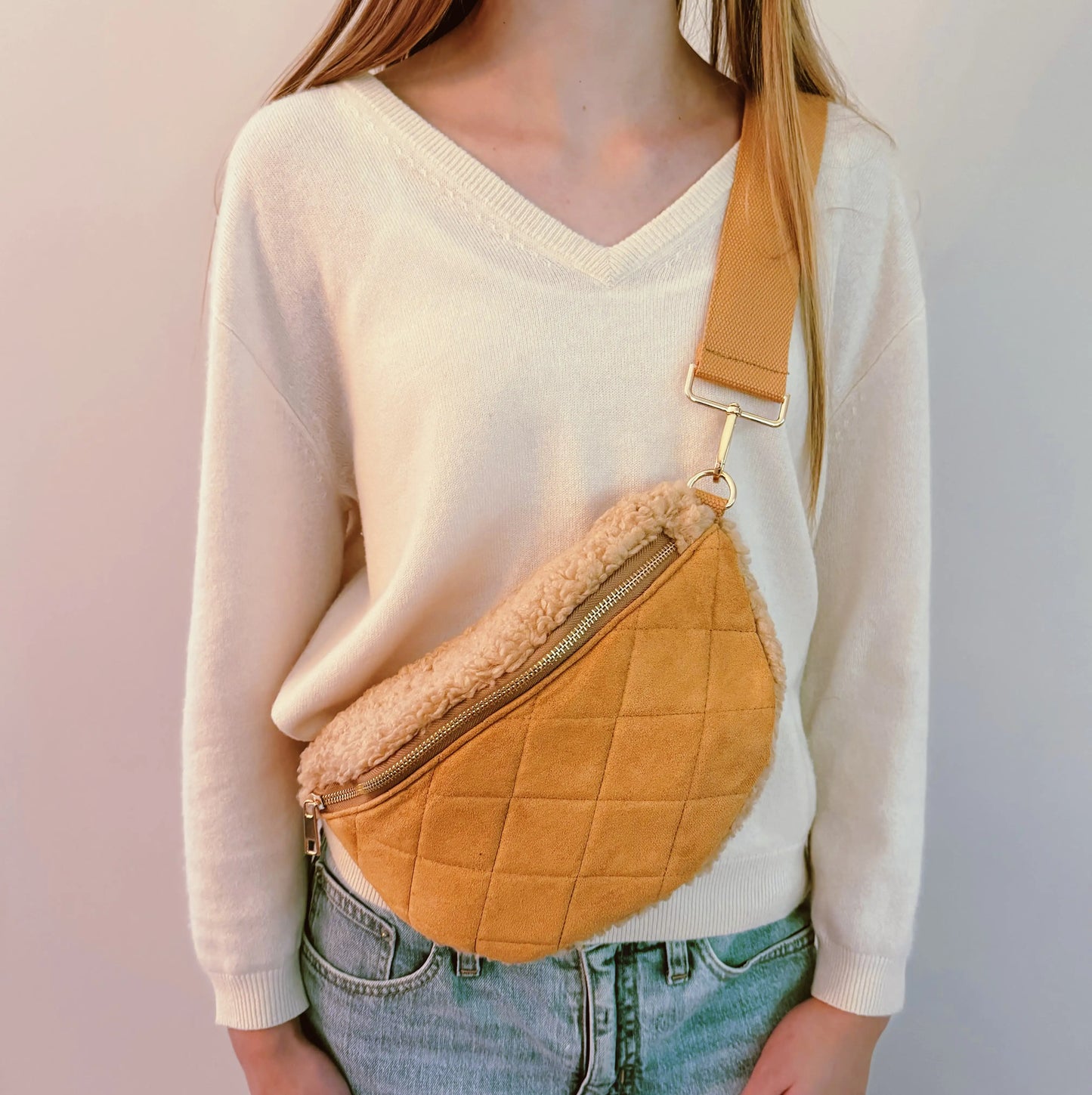 Person wearing a mustard yellow quilted crossbody bag with shearling lining on a plain background