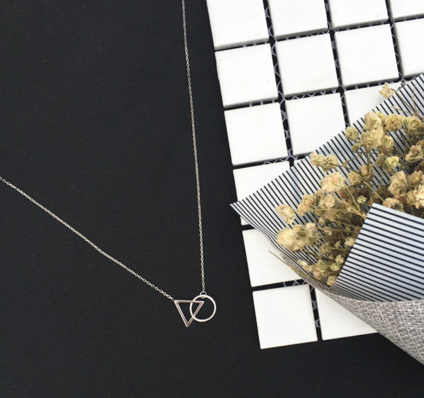 Silver necklace with a geometric pendant on a black surface with a white grid background