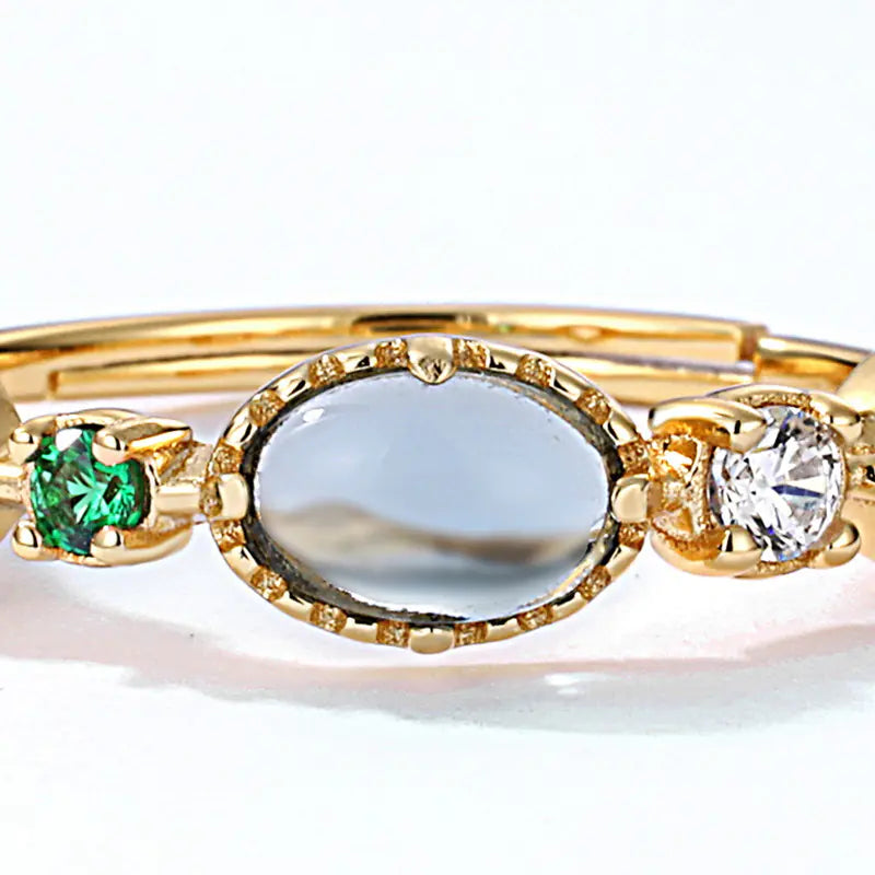 Gold ring with green gemstone, clear stone, and diamond on a white background