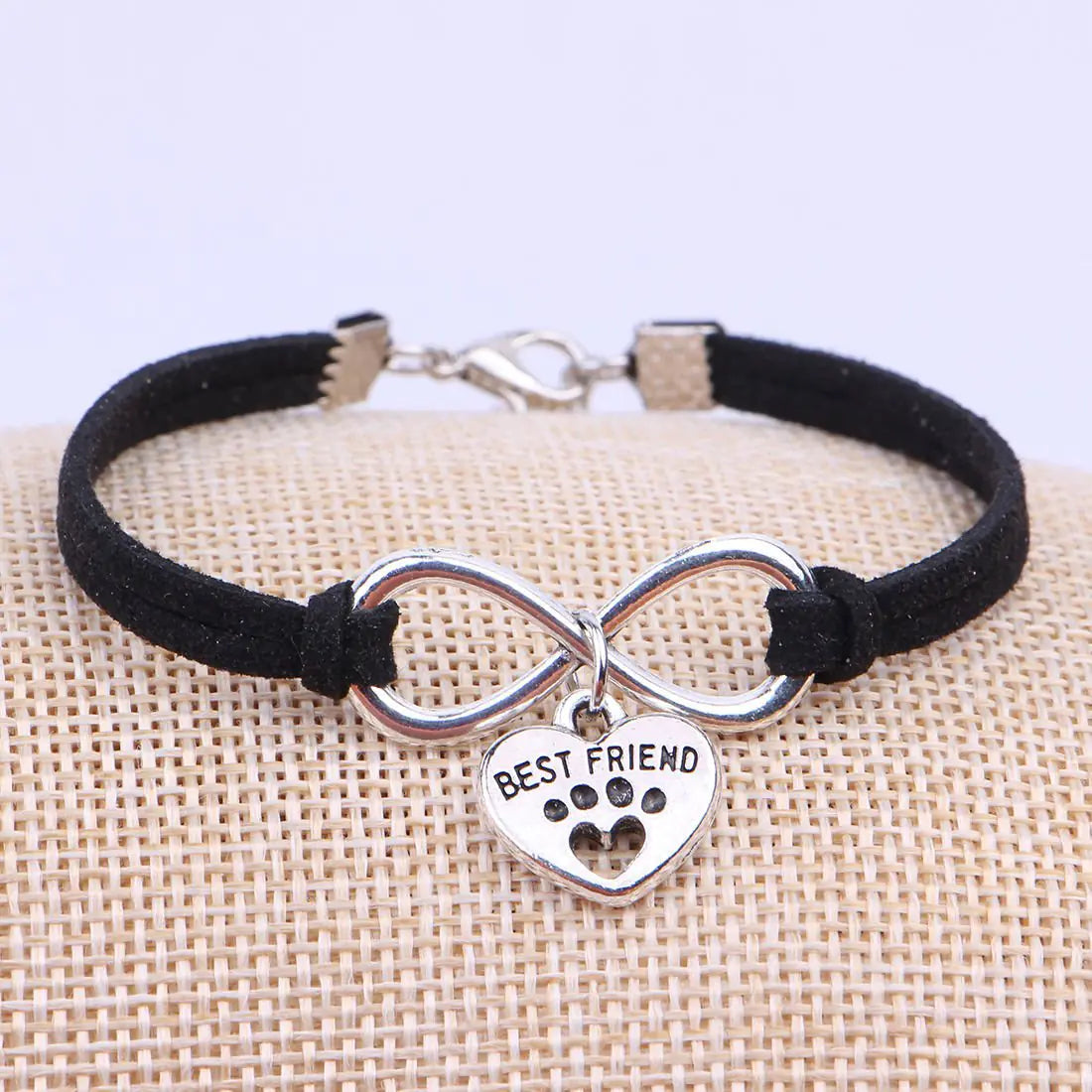 Black bracelet with silver infinity charm and 'Best Friend' heart charm on a textured surface