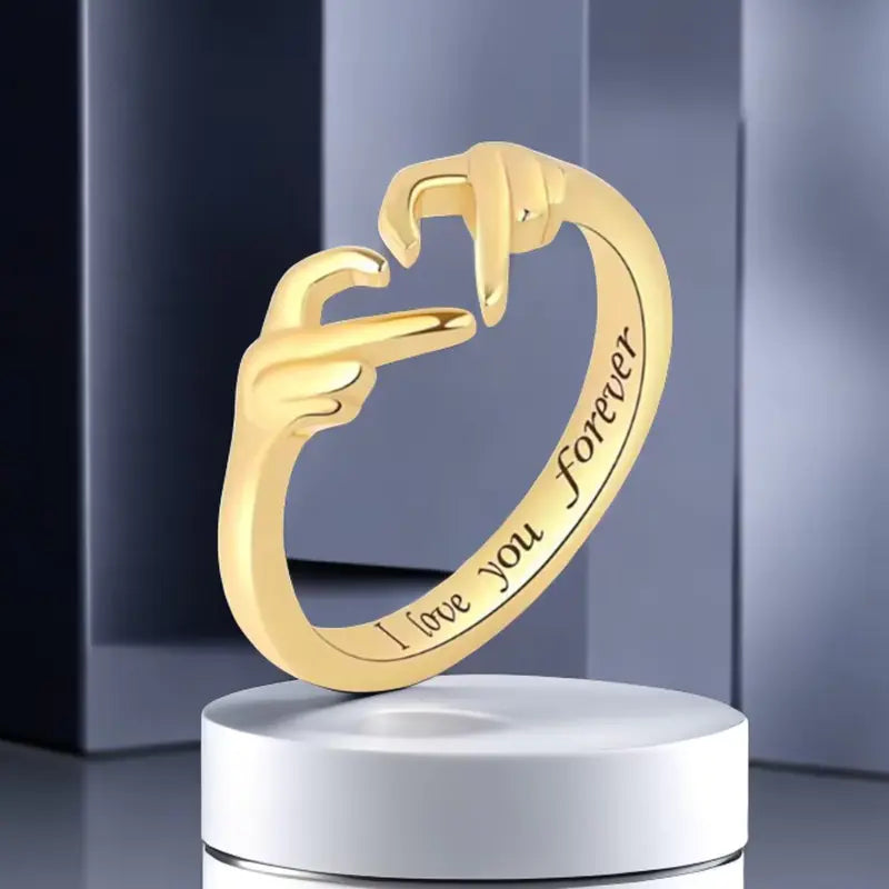 Gold ring with 'I love you forever' engraving on a white stand against a gray background