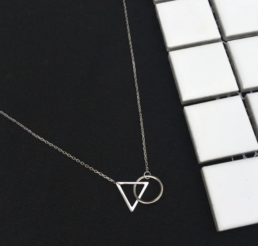 Silver necklace with geometric pendant on a black surface next to a keyboard