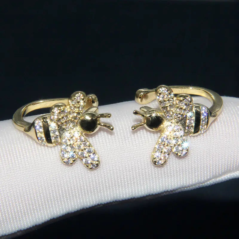 Gold bee-shaped earrings with clear gemstones on a white cushion against a black background