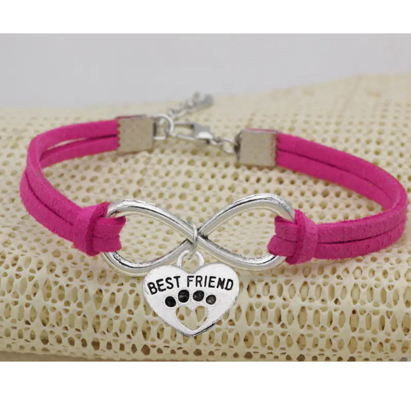 Pink bracelet with silver infinity symbol and 'Best Friend' heart charm on a textured beige surface