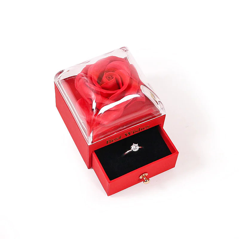 Red rose in a transparent box with a diamond ring inside on a white background