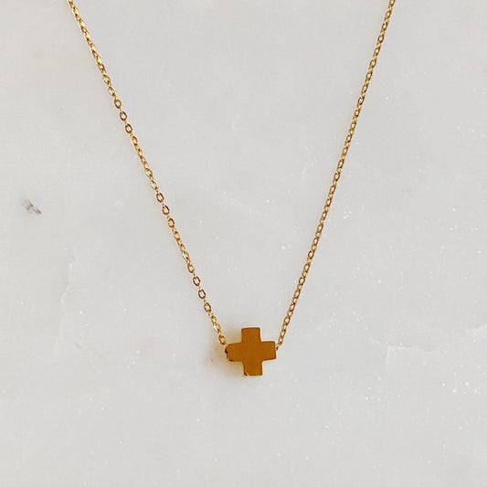 Gold cross necklace on a light gray background