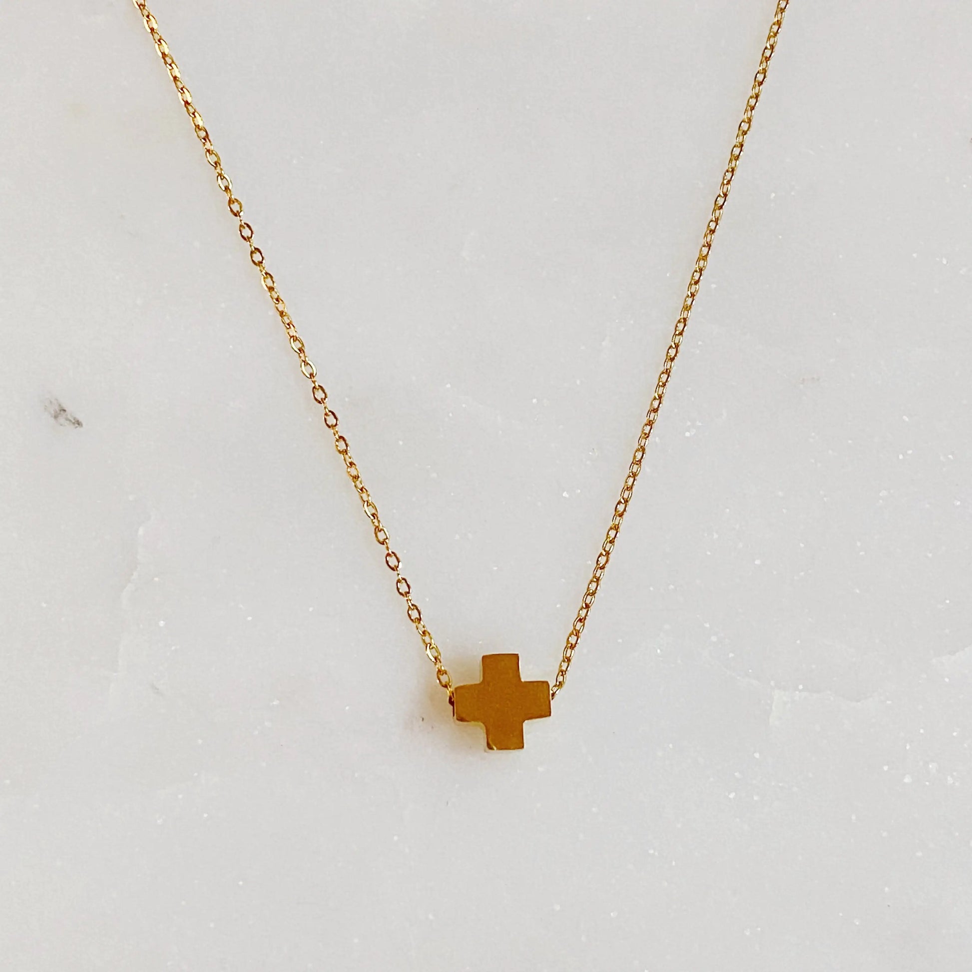 Gold cross necklace on a light gray background
