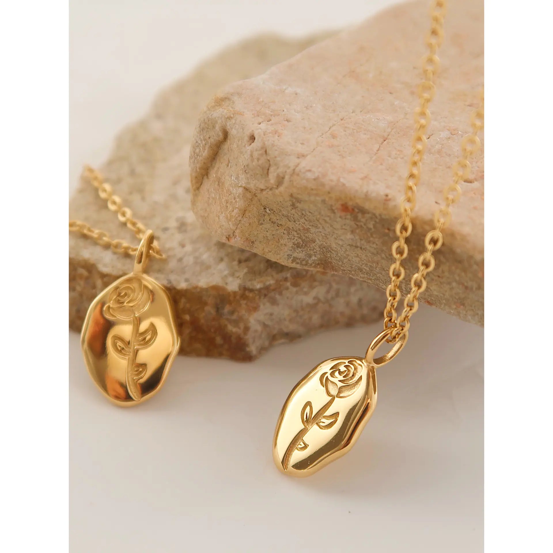 Gold necklaces with rose pendants on a stone surface