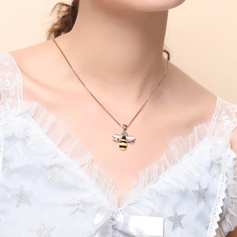 Necklace with a bee pendant worn by a person in a white lace top.