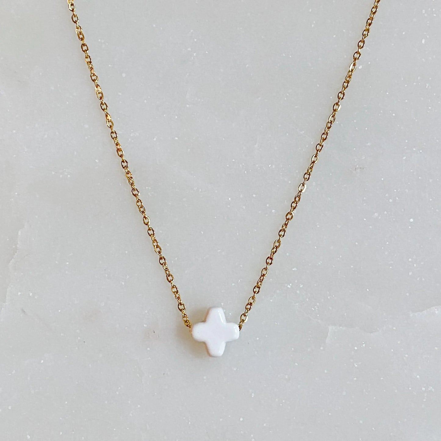 Gold necklace with a white pendant on a gray background
