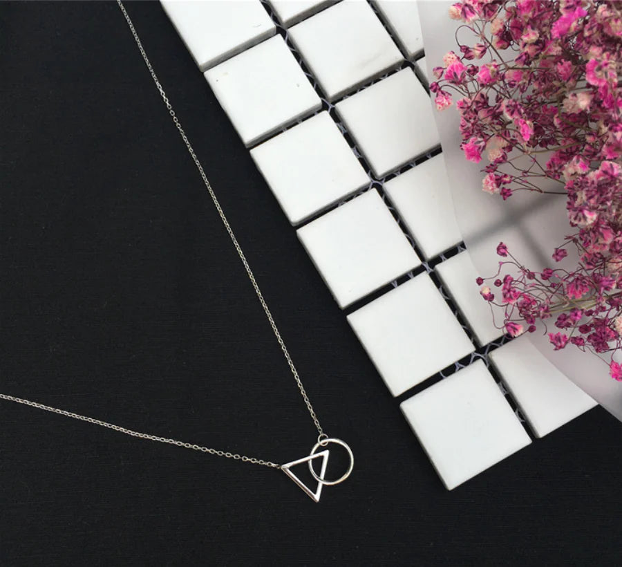 Silver necklace with a geometric pendant on a black and white checkered surface with pink flowers.