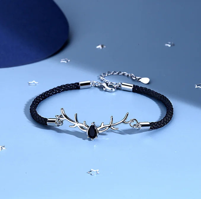 Bracelet with black cord and silver deer antler design on a blue background