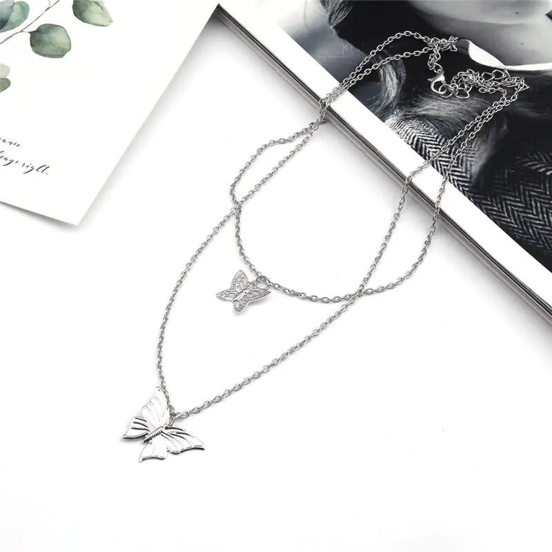 Silver butterfly necklace on a white surface with a magazine in the background