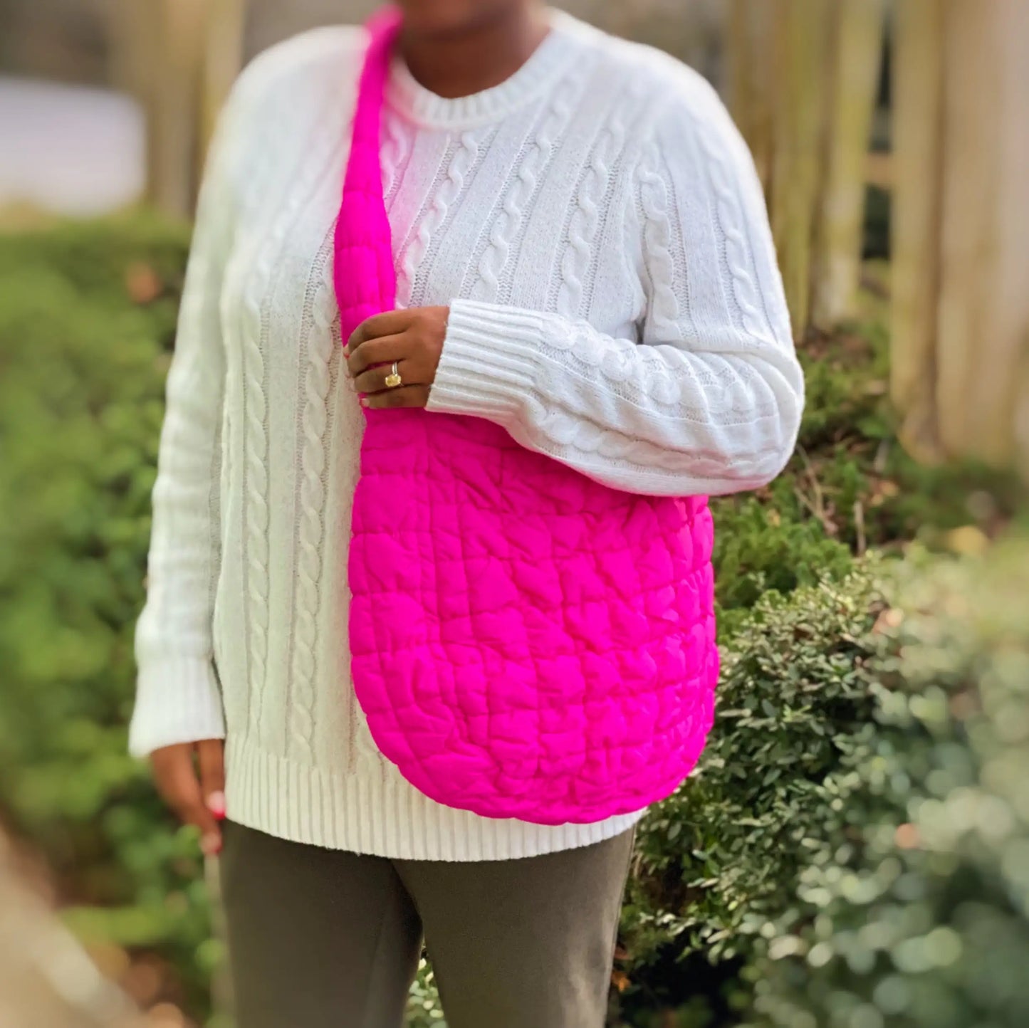 Person wearing a white sweater holding a bright pink textured bag outdoors.