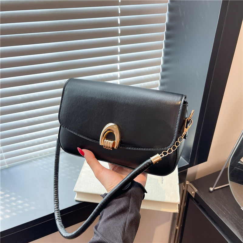 Black handbag with gold clasp held by a person in front of a window.