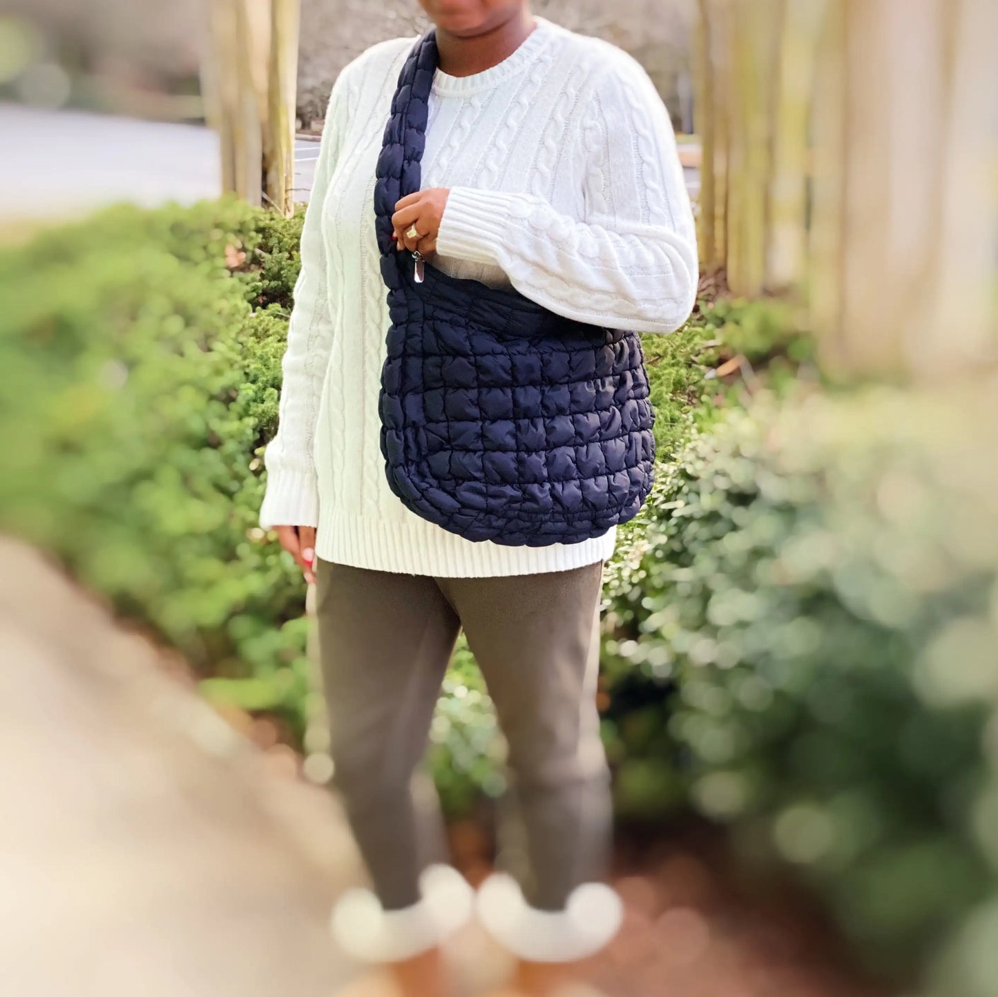 Person wearing a white sweater and holding a navy quilted bag outdoors.