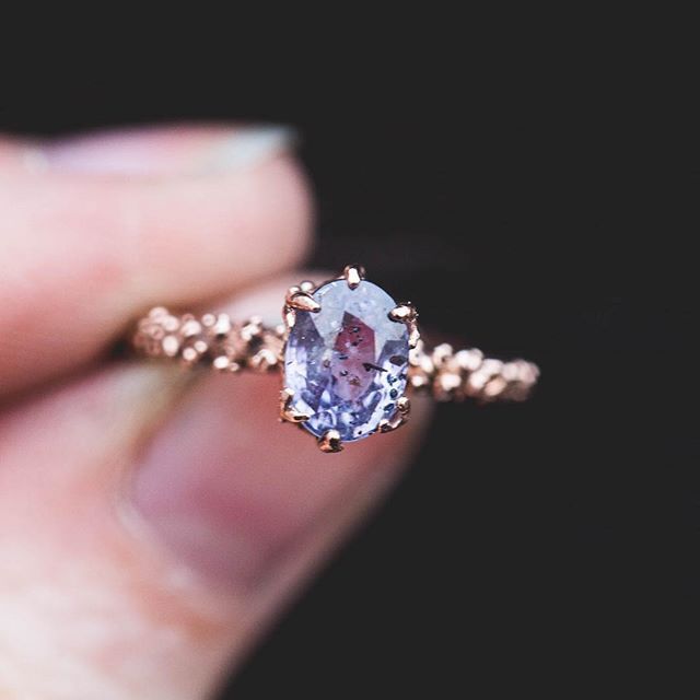 Rose gold ring with a purple gemstone held by a hand against a dark background