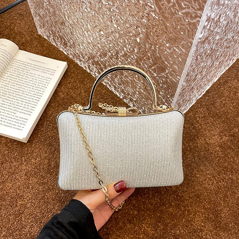 Beige handbag with gold chain held by a hand on a brown surface with an open book.