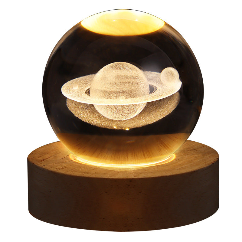 Glass sphere with a model of Saturn on a wooden base against a white background