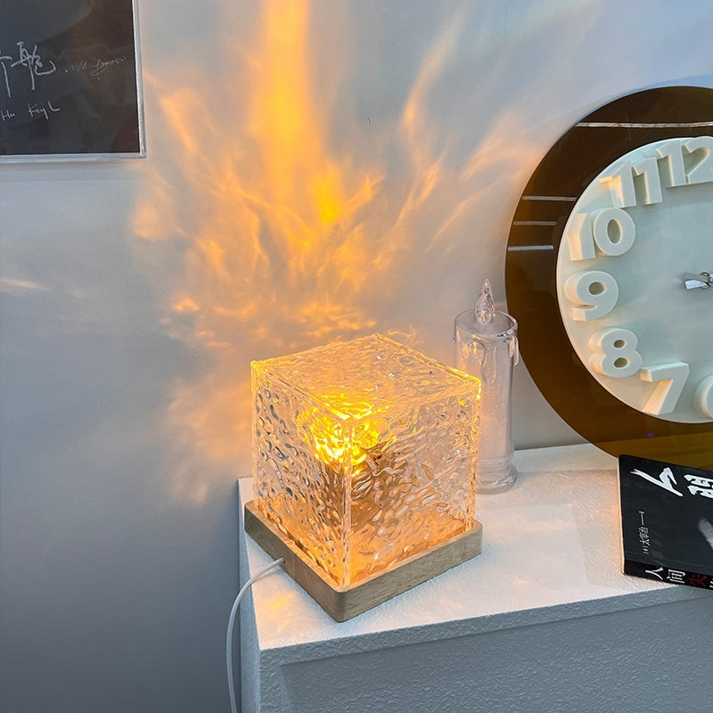 Decorative glass cube light on a shelf with a clock and other items in the background.