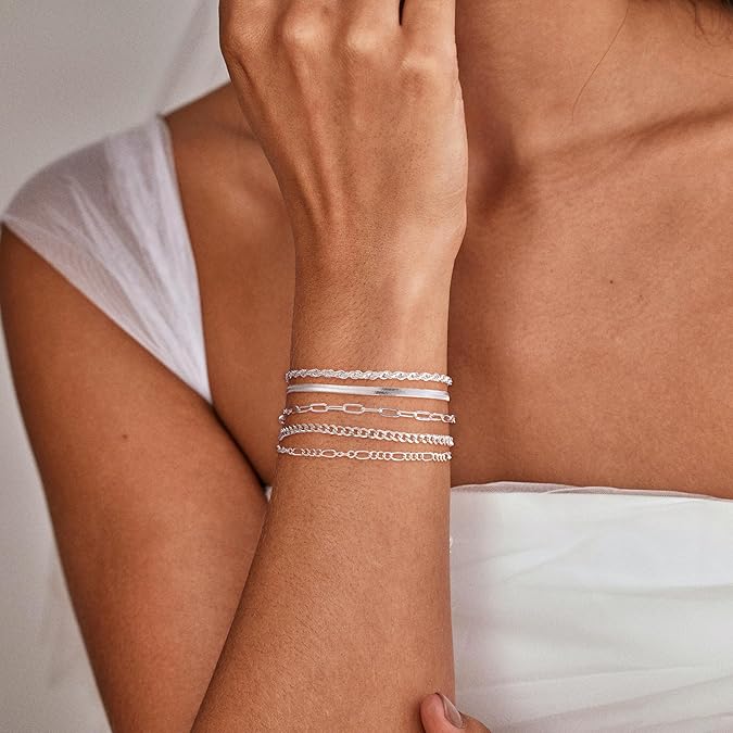 Close-up of a person's arm wearing multiple silver bracelets on a neutral background