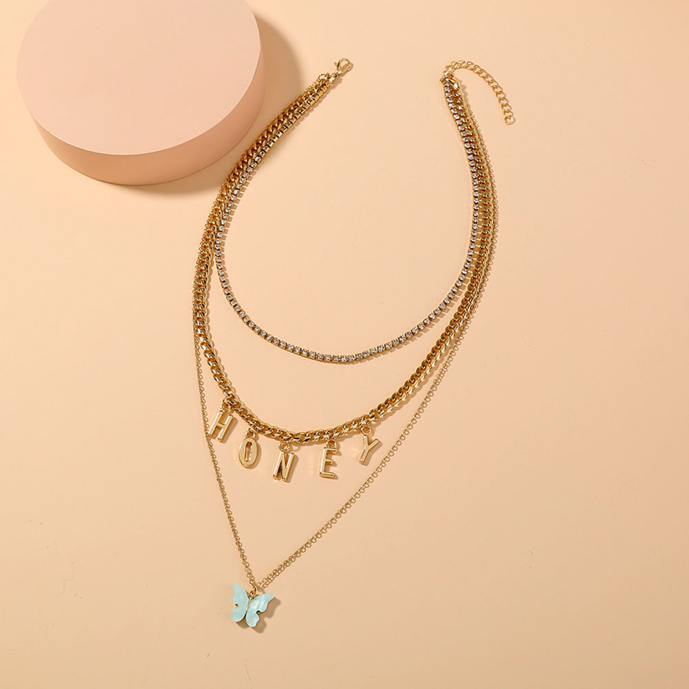 Gold necklace with 'HONEY' and butterfly pendant on a beige background