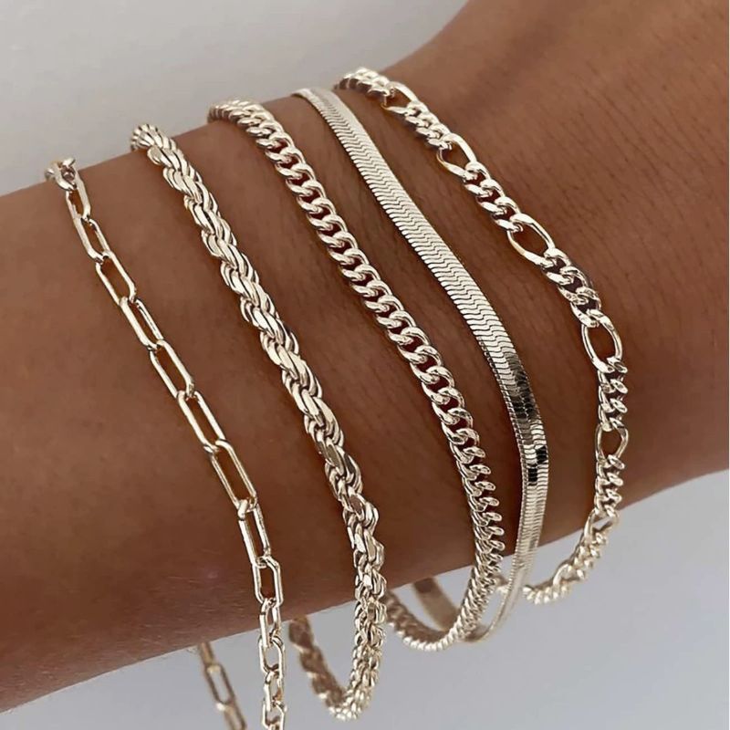 Gold chain bracelets on a wrist against a neutral background