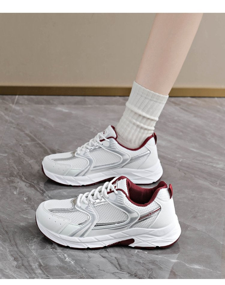 White sneakers with red soles worn by a person on a gray floor.