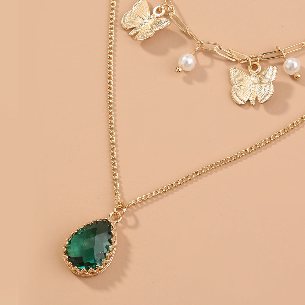 Gold necklace with green teardrop pendant and butterfly charms on a beige background