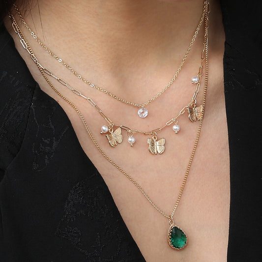 Gold necklaces with butterfly and green teardrop pendants on a person wearing a black top.
