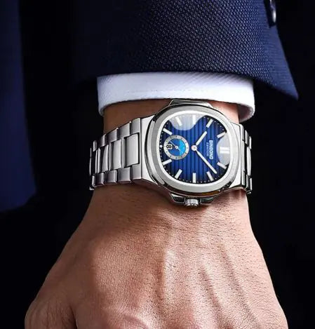 Close-up of a hand wearing a silver watch with a blue face, set against a dark background.